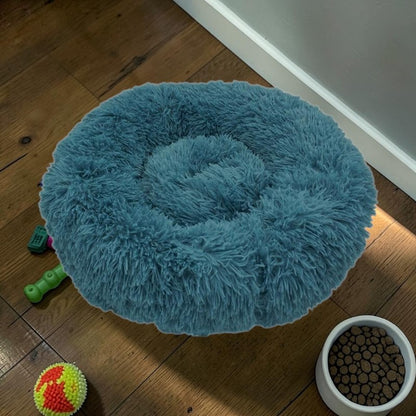 Furvana blue plush donut dog bed with raised rim for orthopedic support on a wooden floor