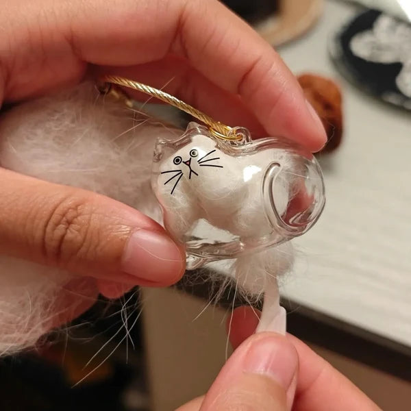 Furvana cat-shaped clear glass keychain being filled with white cat fur as a sentimental pet keepsake