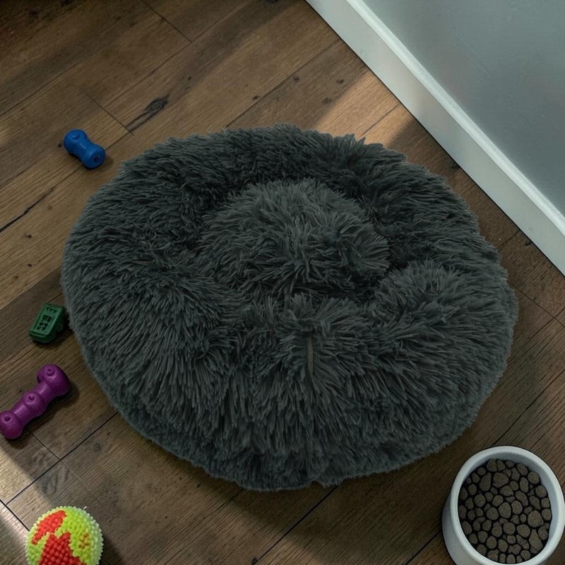 Furvana dark grey plush donut bed for dogs and cats with a raised rim for orthopedic support on a wooden floor