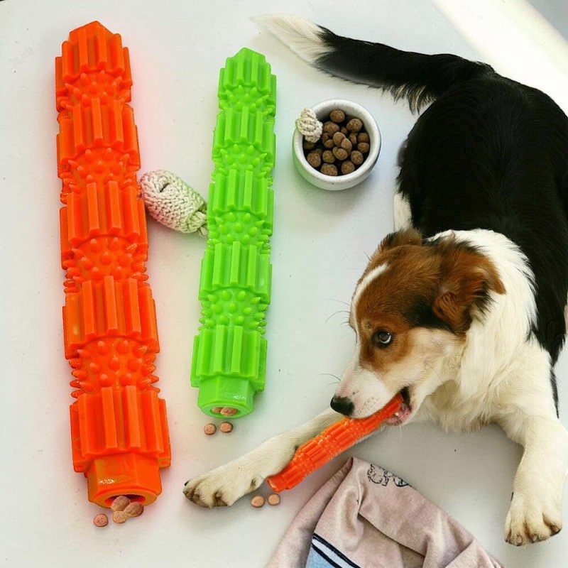 Furvana dog chewing on an orange silicone molar cleaning stick with a green toy and bowl of kibble nearby