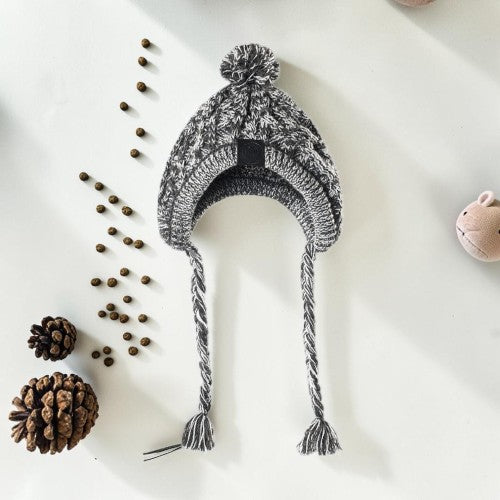 Furvana grey and white marled cable-knit dog hat with ear flaps, braided tassels, and a pom-pom on top.