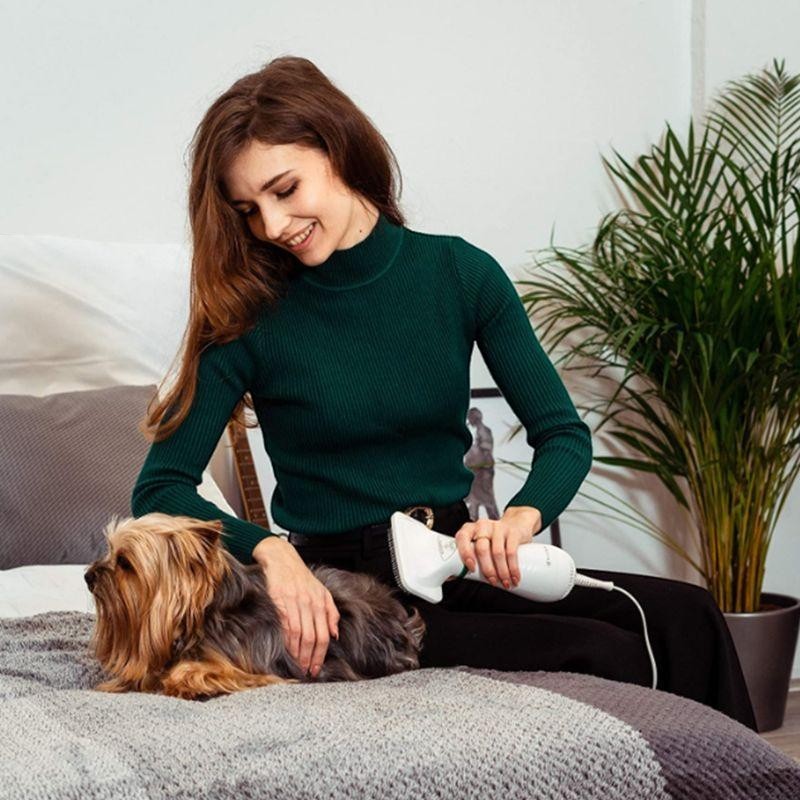 Furvana 2-in-1 pet dryer brush being used by a woman to groom a small dog on a bed