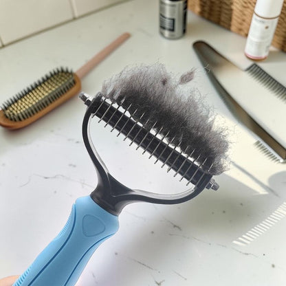 Furvana pet knot remover comb with stainless steel teeth holding a clump of removed grey dog fur on a white surface