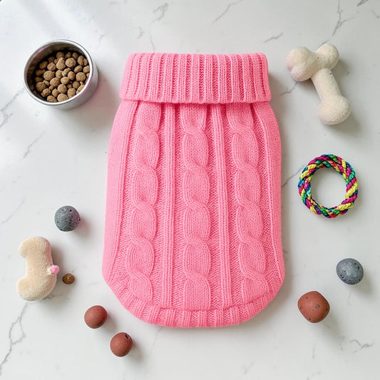 Furvana pink cable knit turtleneck pet sweater laid flat on a white surface with dog toys and food bowl