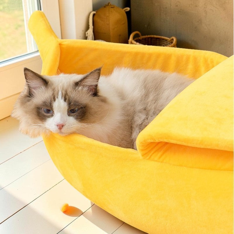 Furvana yellow banana-shaped plush pet bed with a fluffy cat resting inside on a wooden floor