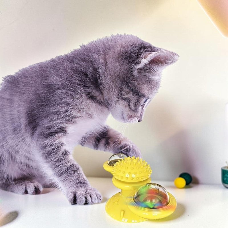 A grey kitten playing with a yellow Furvana windmill cat toy featuring spinning compartments and a suction base